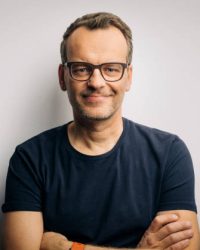 Portrait of confident mature man in t-shirt. Smiling handsome male is wearing eyeglasses. He is with arms crossed against white background.